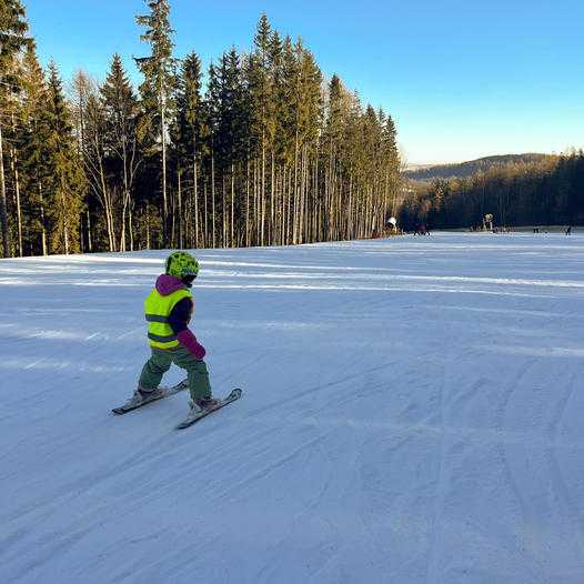 Malý lyžař jede před instruktorem lyžování. 